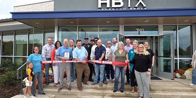 Group of people celebrating a ribbon-cutting event outside a bank.