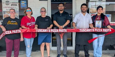 Group of six people cutting a red ribbon for Tuscany's Pizza Pasta opening.