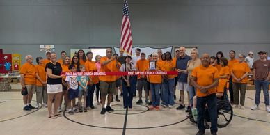 Group of people in orange shirts holding a red banner inside a gym.