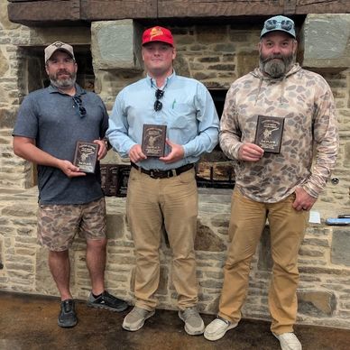 Three men holding awards in front of a stone fireplace.