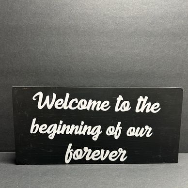 Black sign with white text reading 'Welcome to the beginning of our forever'.