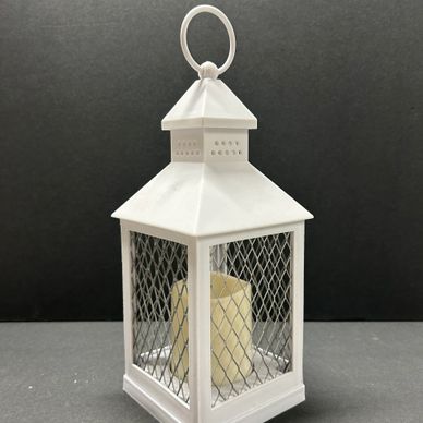 White metal lantern with a faux candle inside on a gray surface.