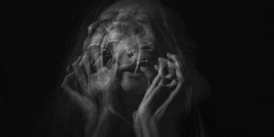 Black and white image of a person with multiple blurred faces expressing anguish.