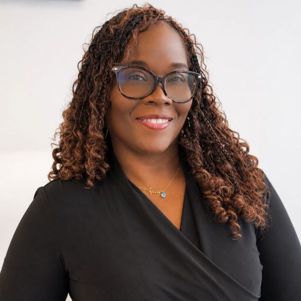 Confident woman with curly hair and glasses smiling warmly.