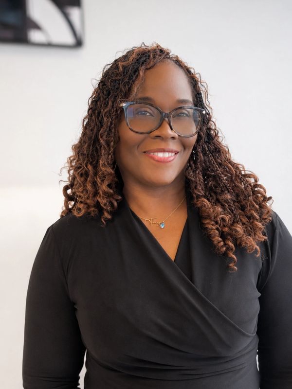 Smiling woman with curly hair and glasses in a black top.
