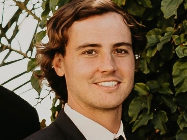 Young man smiling in formal attire outdoors.