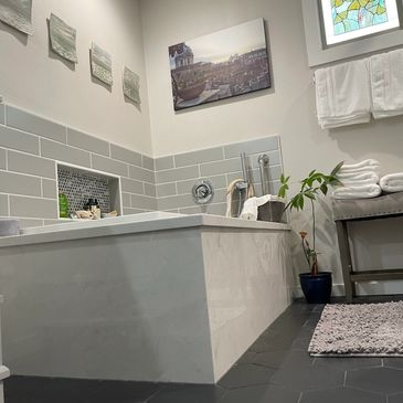 Modern bathroom with a soaking tub, gray tiles, and artistic decor.