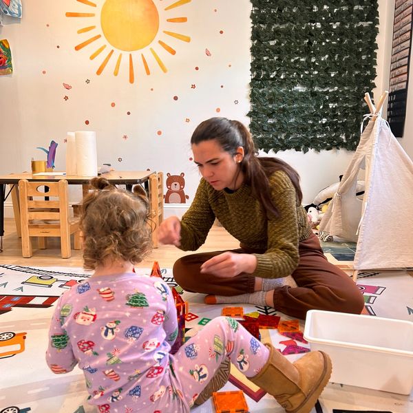 Child and adult playing with colorful blocks in a bright, decorated room.
