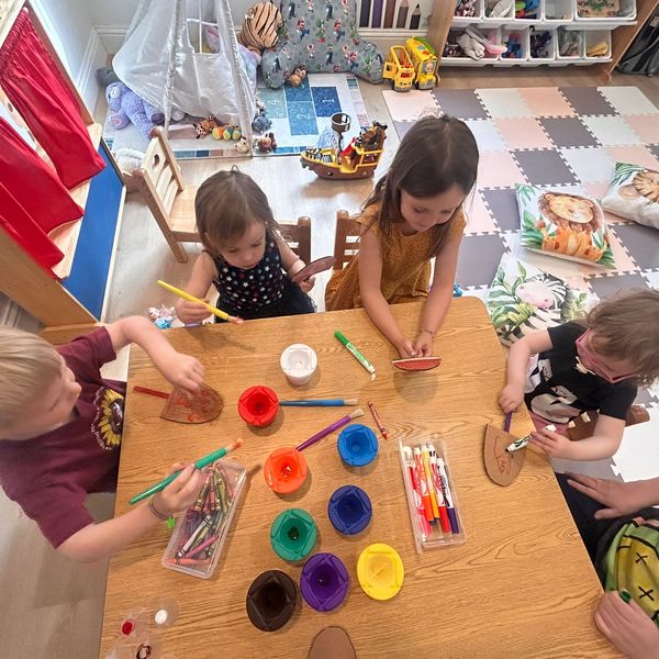 Four young children engaged in a colorful arts and crafts activity at a wooden table.