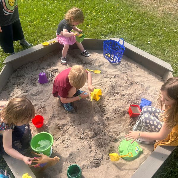 Children playing with sand and toys in a sandbox outdoors on a sunny day.