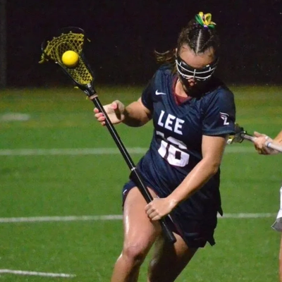Female lacrosse player in action with ball in stick net.
