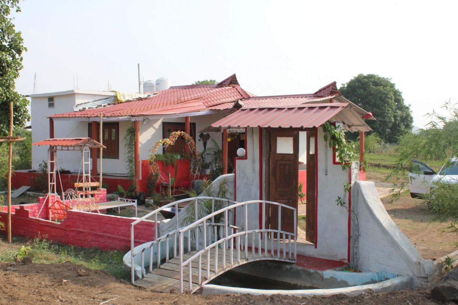 A quaint house with a red roof and a small white bridge in front.