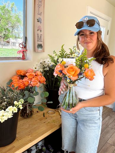 Woman holding a vase with a bouquet of orange roses and greenery indoors.