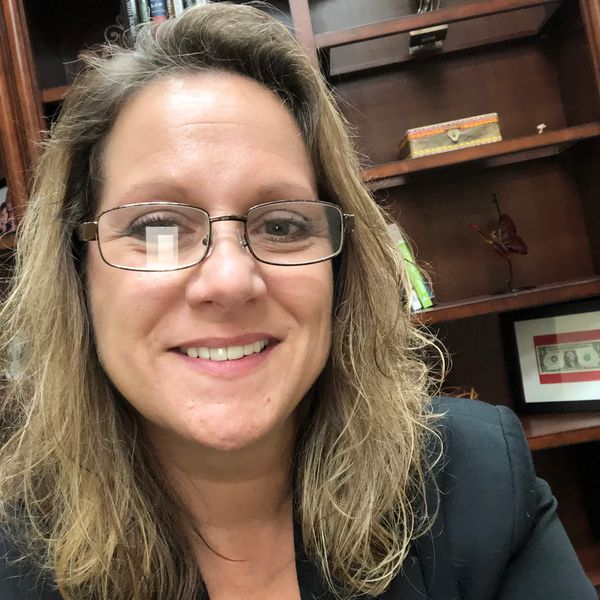 Smiling woman with glasses in an office setting.