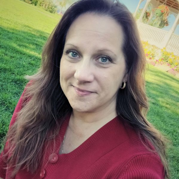 Woman in red sweater smiling outdoors near a white gazebo.