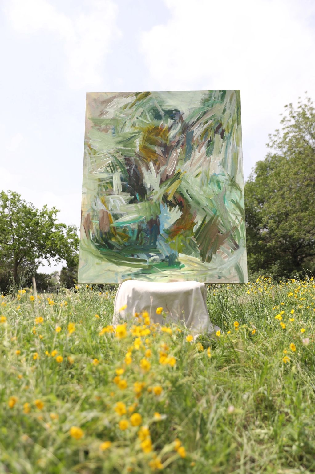Abstract painting displayed outdoors in a field of yellow flowers.