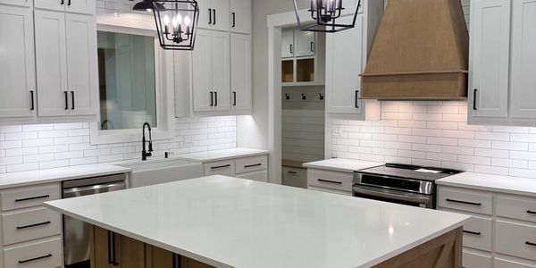 Modern kitchen with white countertops, wooden island, and black pendant lights.
