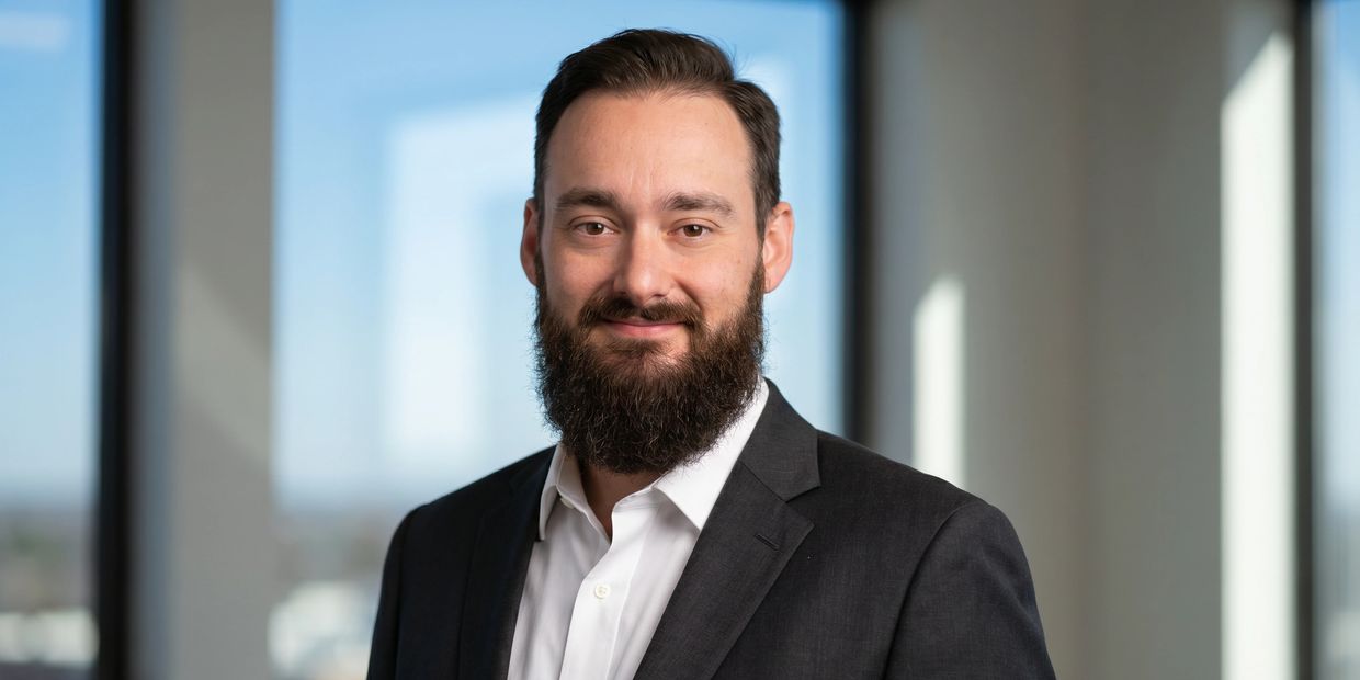 Confident man in a suit with a beard smiles warmly indoors.