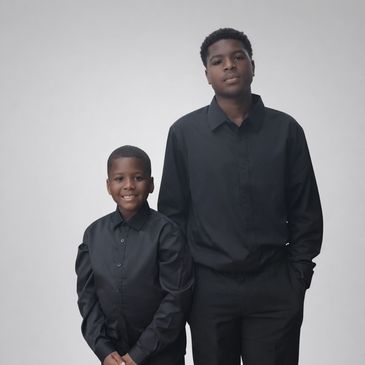 Two brothers dressed in black shirts and pants posing against a plain background.