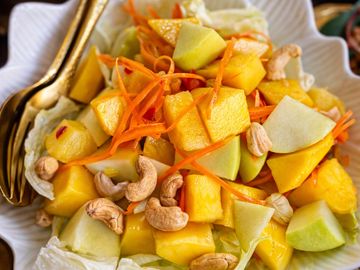 A fresh fruit and cashew nut salad with carrots on a white plate.