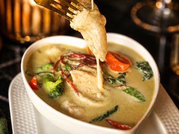 A bowl of creamy Thai green curry with chicken and vegetables.