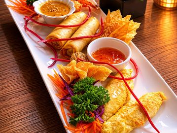 A colorful platter with spring rolls, dipping sauces, and garnishes on a wooden table.