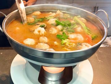 Hot pot filled with vegetables and meatballs, kept warm by a flame underneath.