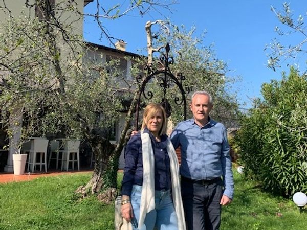 A couple standing outdoors near a decorative wrought iron structure on a sunny day.