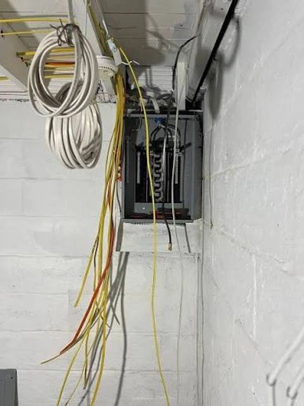 Electrical panel with hanging cables in a white-walled room.
