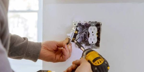 Person installing an electrical outlet using a power drill.