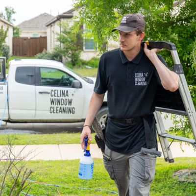 Window cleaner carrying ladder and spray bottle near branded truck.