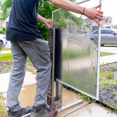 Person cleaning a large solar panel with a specialized cleaner outdoors.