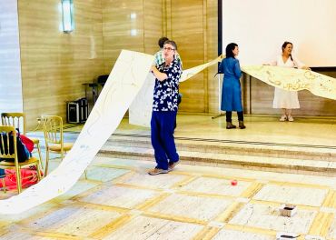 People holding a long scroll in a room.