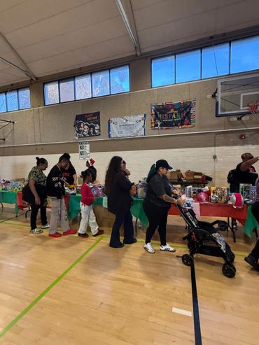 People lined up at a community event in a gymnasium with tables of items.