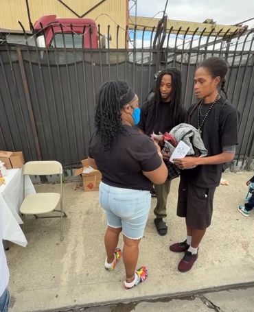 Three people conversing outdoors near a fence, one woman wearing a face mask.