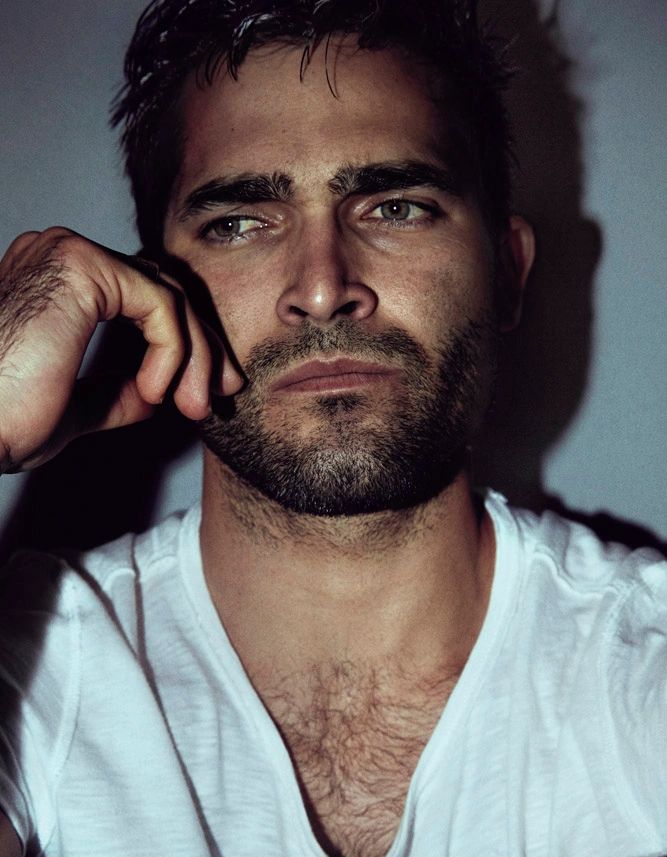 Close-up of a pensive man with a beard in a white shirt.