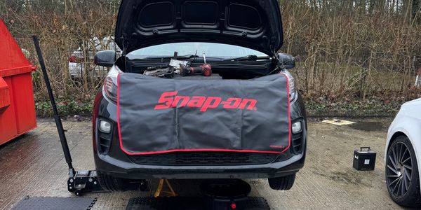 Car with open hood being repaired outdoors.