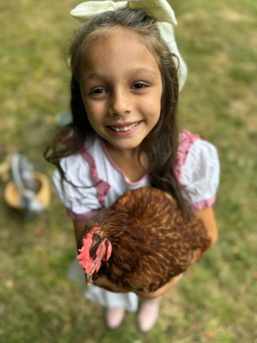 Young girl smiling while holding a brown chicken outdoors.