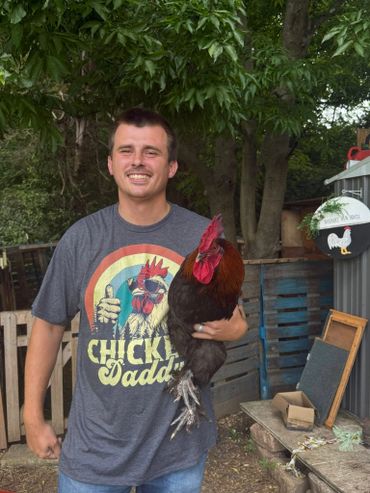 Man smiling, holding a rooster, wearing a "Chicken Daddy" shirt.
