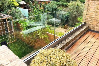 Modern glass balcony overlooking a lush backyard garden.