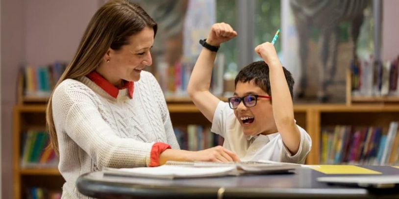 Teacher and student celebrating success at table.