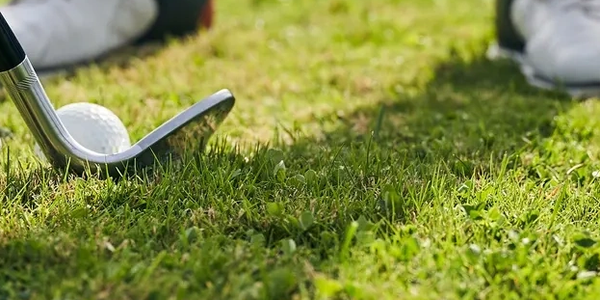 Golf club hitting golf ball on grass.