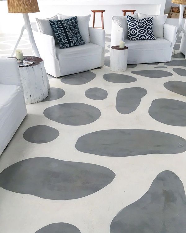 Modern sitting area with white chairs and patterned pillows on a unique spotted floor.