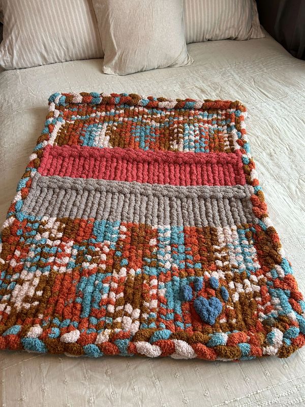 Colorful, textured crochet blanket with heart detail on bed.