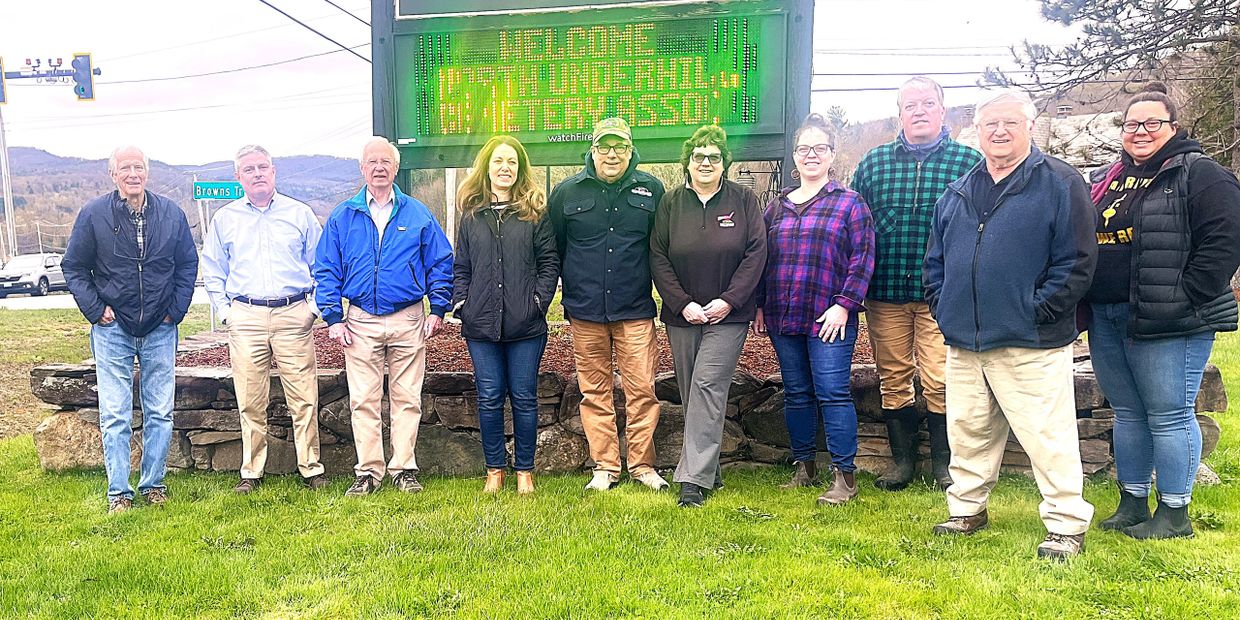 Group of people standing in front of a welcome sign outdoors.