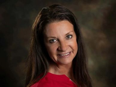 Woman with long dark hair smiling against a dark background.