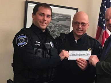 Two police officers and a man holding a certificate or check indoors.