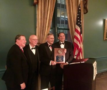 Four men in tuxedos posing with an award plaque at a formal event.