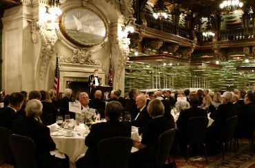 Elegant formal dinner event with a speaker addressing guests in a grand hall.
