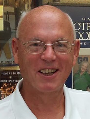 Smiling elderly man wearing glasses and a white shirt.